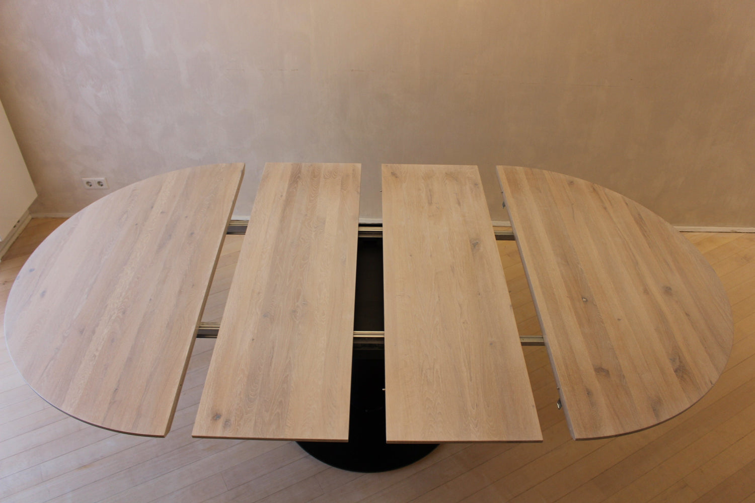Contemporary round oak dinner table with hidden extension and powder-coated black legs